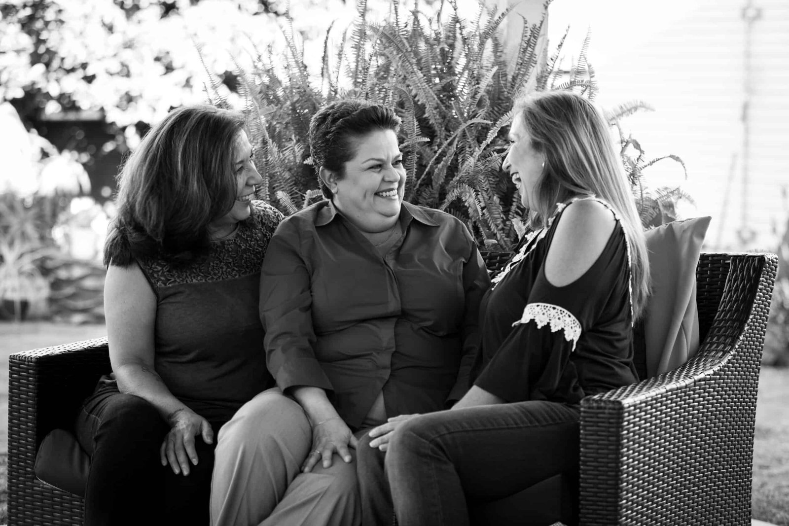 Three women sitting on a bench talking to each other.