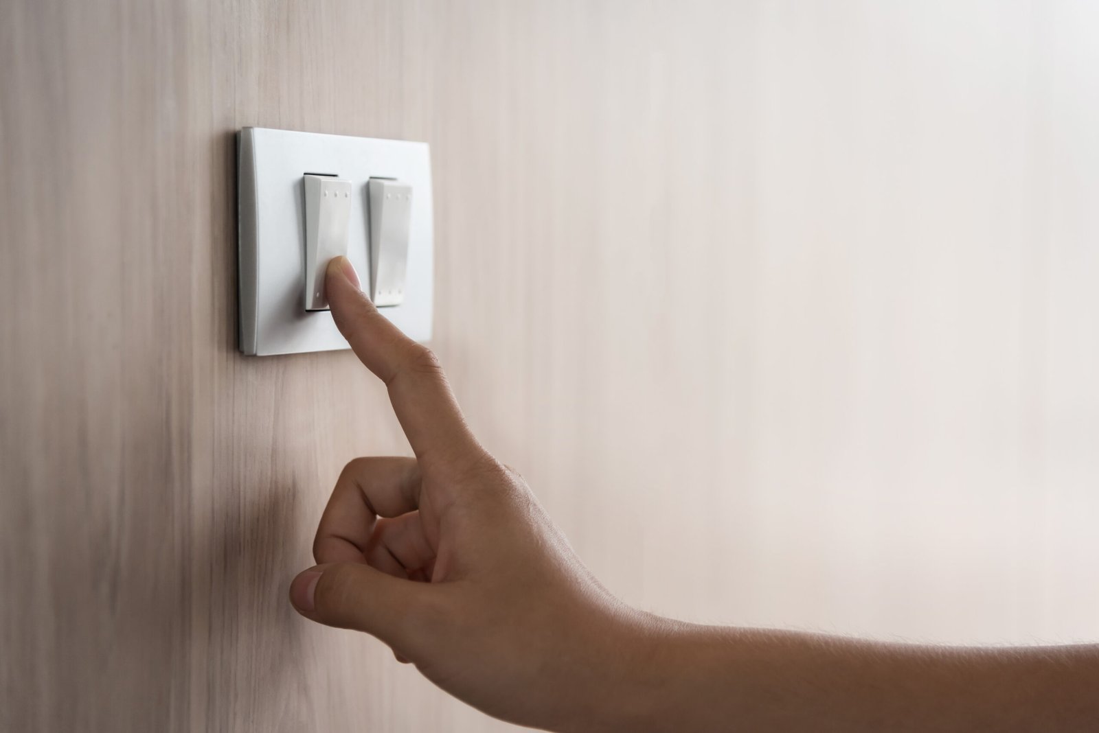 Close up hand turning on or off on grey light switch with wooden A hand is pointing to the light on a wall.