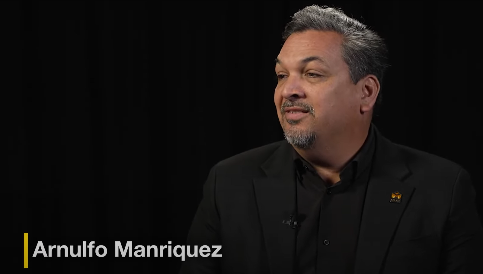 A man in black jacket and shirt sitting down.