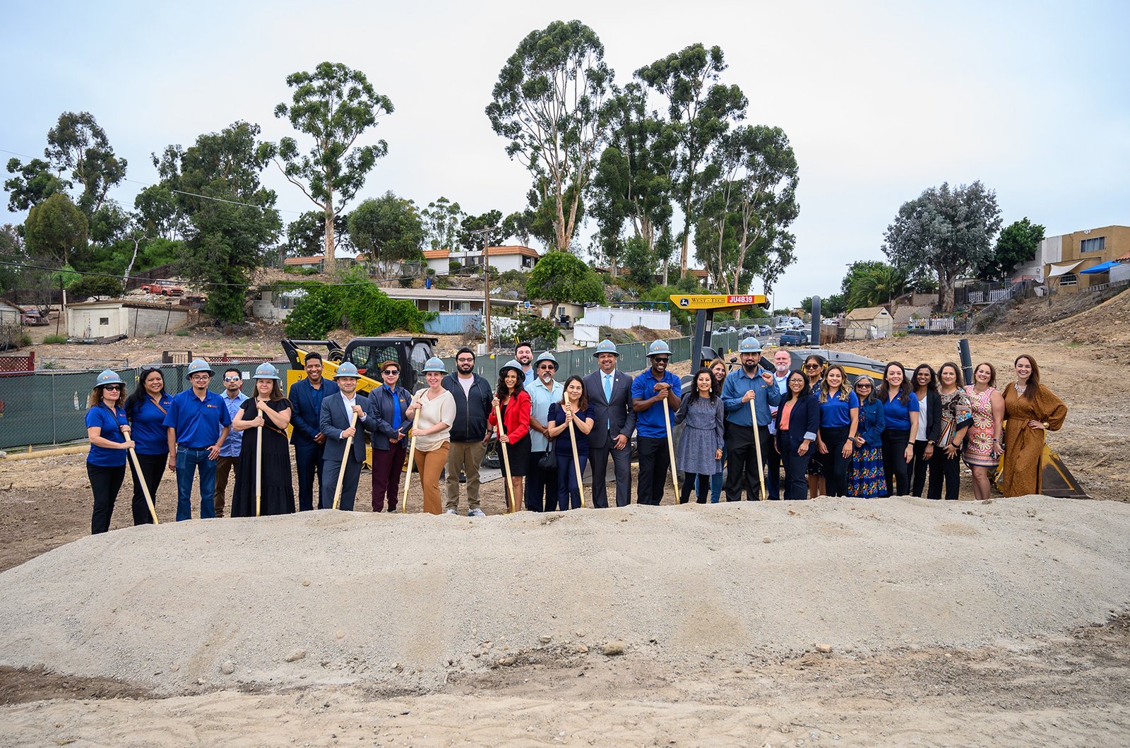 A group of people standing in the sand holding shovels.