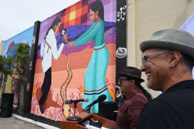 Two men standing in front of a mural.