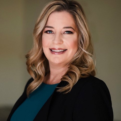 A woman with long blonde hair wearing a black jacket.