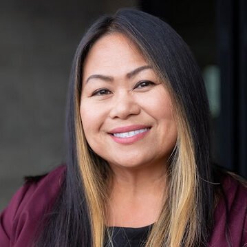 A woman smiling for the camera in front of flowers.