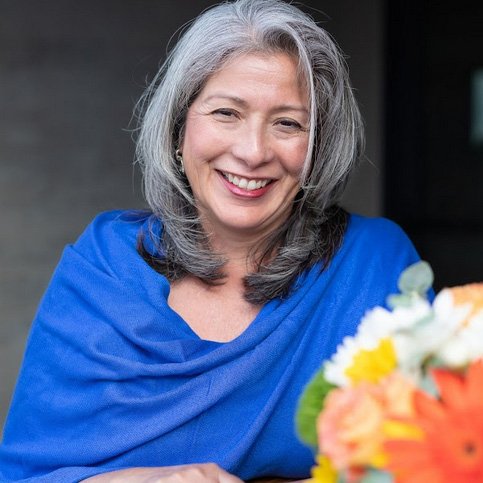 A woman with gray hair sitting in front of flowers.