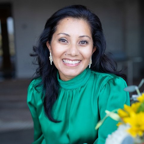 A woman in green shirt holding flowers and smiling.