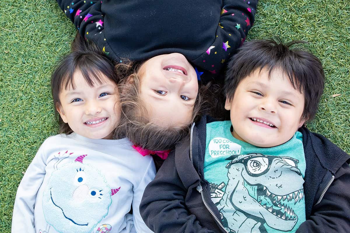 Three children laying on the grass smiling for a picture.