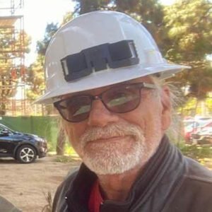 A man with a hard hat on in front of some trees.